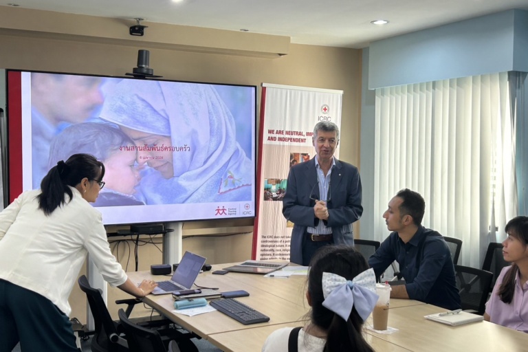 บุคคล 5 คนในห้องประชุมโดยมีผู้ชายยืนพูดอยู่หน้าห้อง